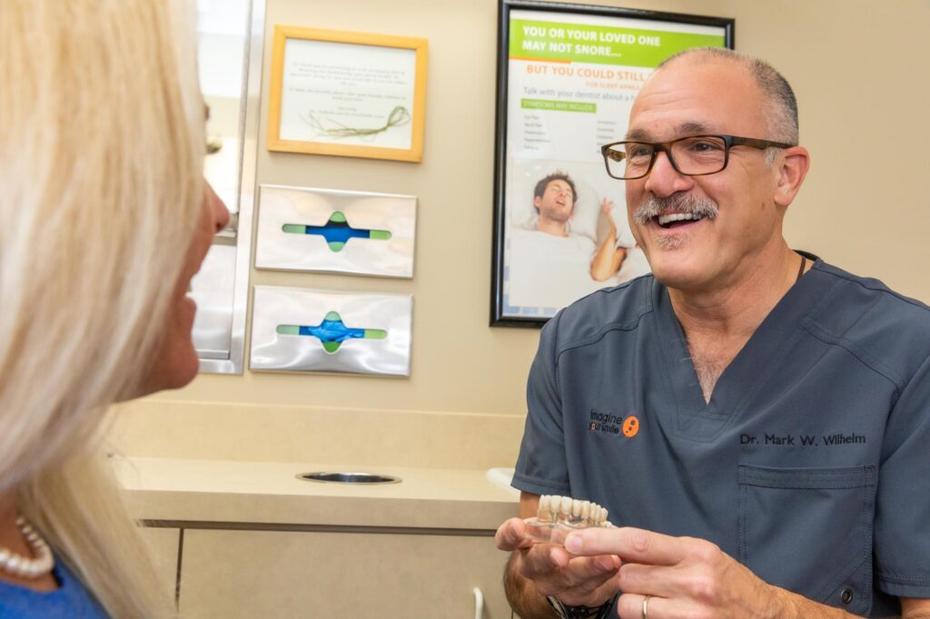 Dr. Wilhelm smiling at a patient while he shows her a dental implant model.