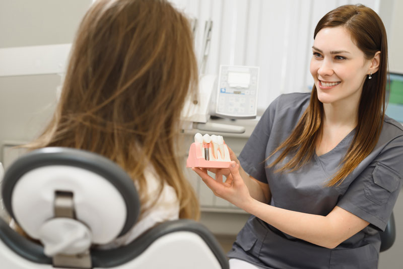 a dental professional using a dental implant model to show a patient in a procedure chair how they can have a new smile in one day with dental implants.