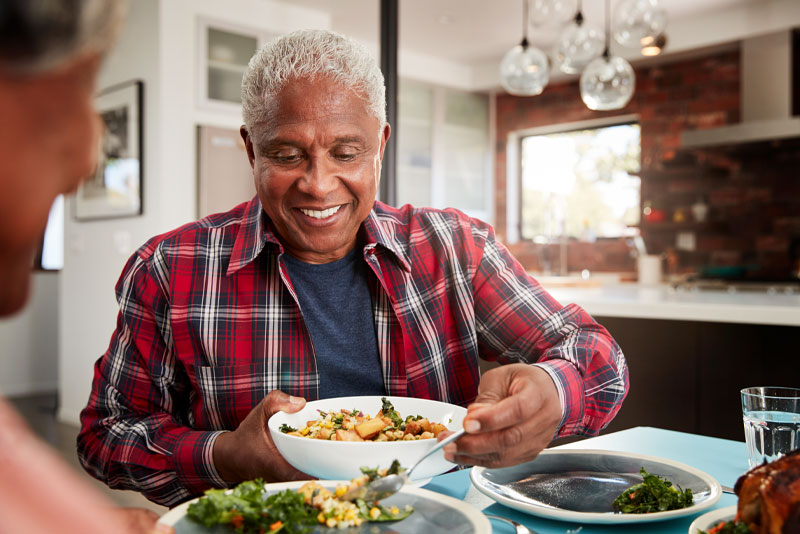 a dental implant patient smiling while he is eating at the dinner table because he could afford the cost of his dental implant procedure.